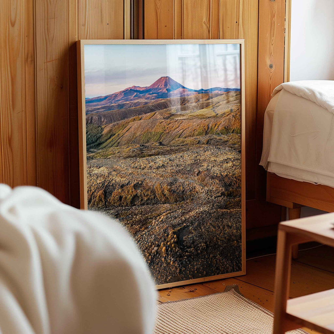 Framed Ruapehu volcanic landscape print in natural wood frame leaning against pine panelled bedroom wall