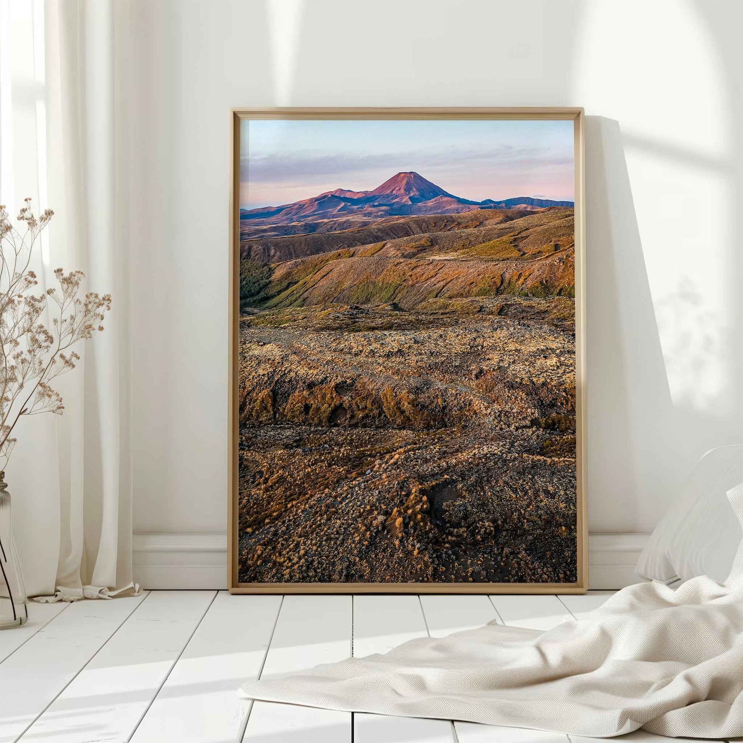 Natural wood framed Ruapehu landscape print leaning against white wall on white floorboards in minimal Scandinavian interior
