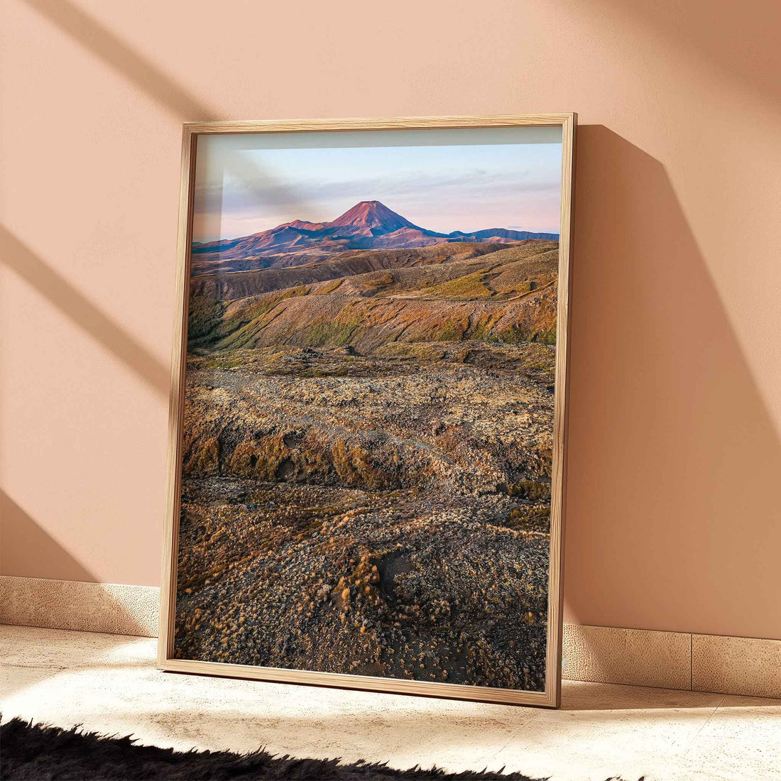 Framed New Zealand volcanic landscape print in light wood frame leaning against terracotta wall with dramatic shadows