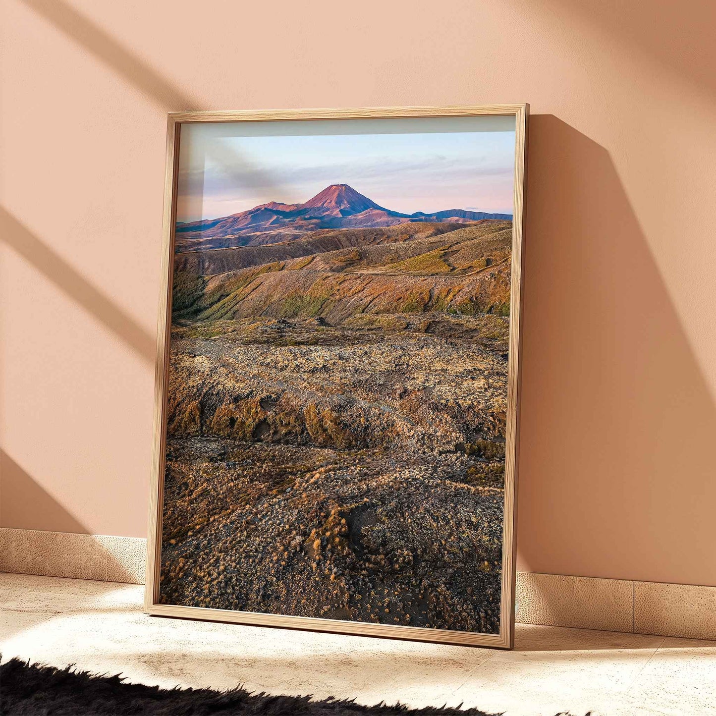 Framed New Zealand volcanic landscape print in light wood frame leaning against terracotta wall with dramatic shadows