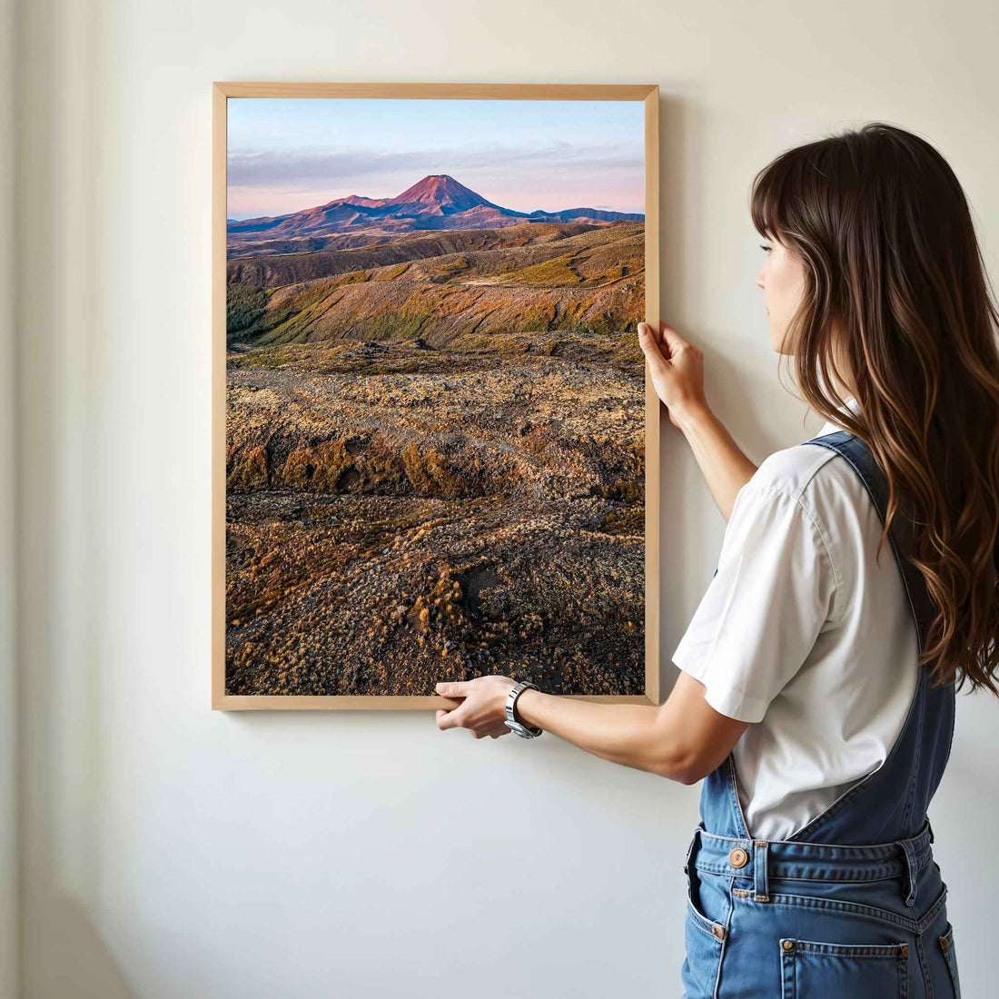 Woman hanging framed Mount Ruapehu landscape photography print in natural oak frame on white wall